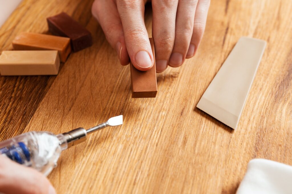 Man heating hard wax for repair cracks, scratches, dents in the wooden floor.