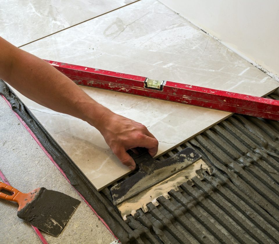 Ceramic tiles and tools for tiler. Worker hand installing floor tiles. Home improvement, renovation